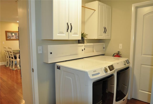 clothes washing area with washing machine and clothes dryer, dark wood-style floors, and cabinet space