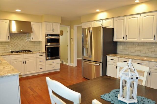 kitchen with tasteful backsplash, white cabinets, ventilation hood, stainless steel appliances, and wood finished floors
