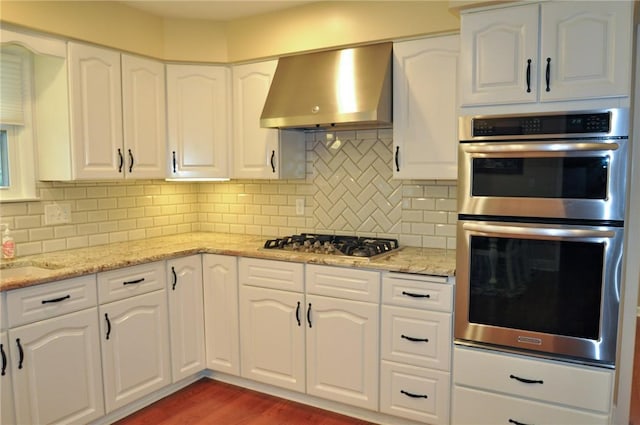 kitchen featuring appliances with stainless steel finishes, decorative backsplash, wall chimney range hood, and wood finished floors