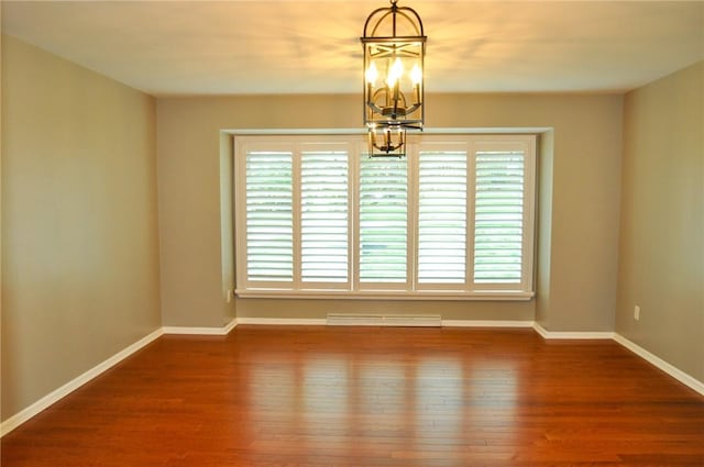 empty room featuring wood finished floors, an inviting chandelier, baseboards, and visible vents