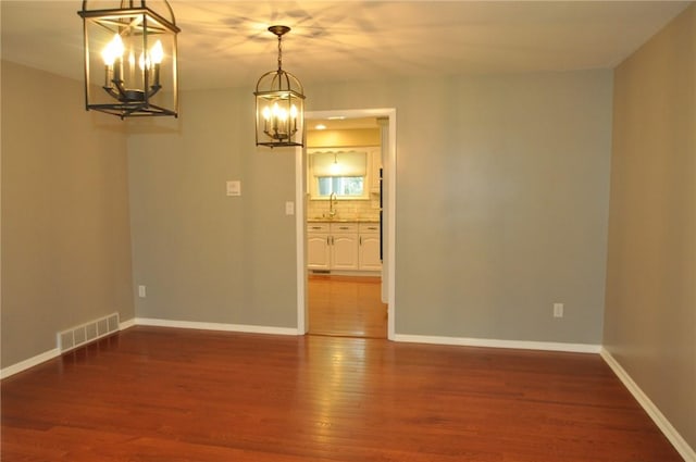 spare room featuring a chandelier, wood finished floors, baseboards, and visible vents