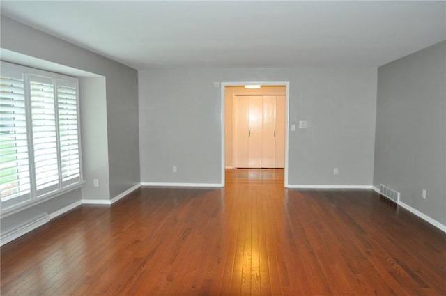 unfurnished room featuring baseboards, wood-type flooring, and visible vents