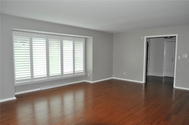 empty room featuring dark wood-type flooring, visible vents, and baseboards