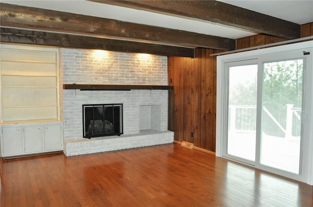 unfurnished living room featuring beam ceiling, wood finished floors, and wood walls