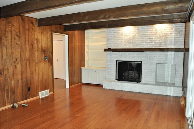 unfurnished living room with wood finished floors, wood walls, beamed ceiling, and visible vents