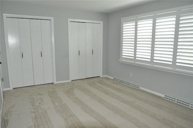 unfurnished bedroom featuring visible vents, carpet, two closets, and baseboards