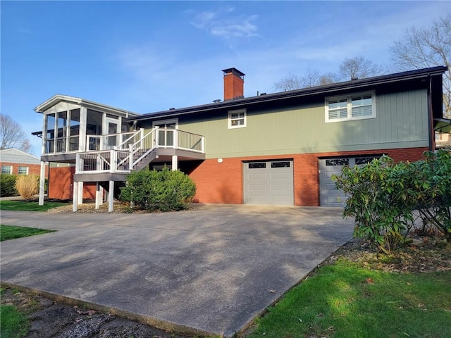 view of front of property with a sunroom, stairway, an attached garage, a chimney, and driveway