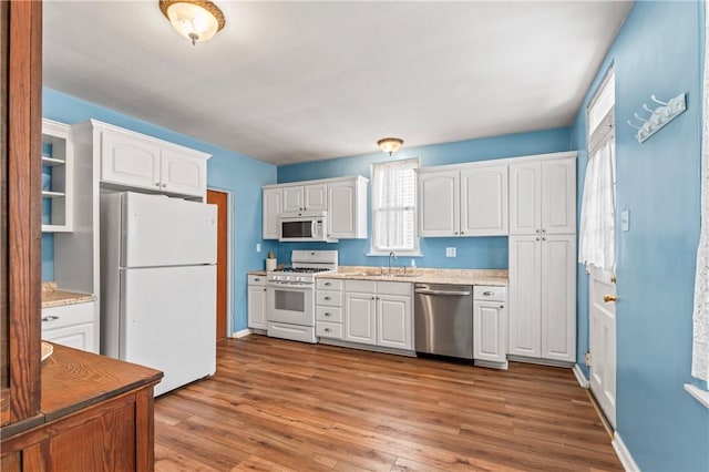kitchen with a sink, light countertops, white appliances, white cabinetry, and wood finished floors