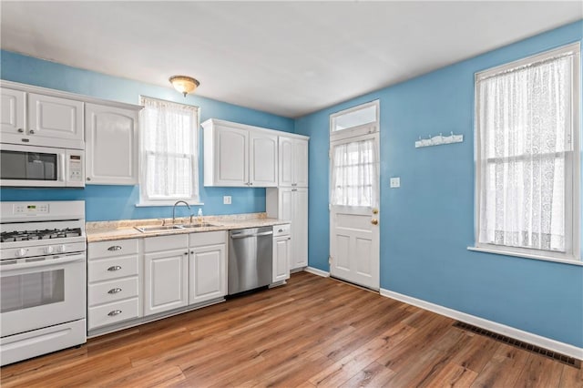 kitchen featuring visible vents, white cabinets, a sink, light wood-type flooring, and white appliances