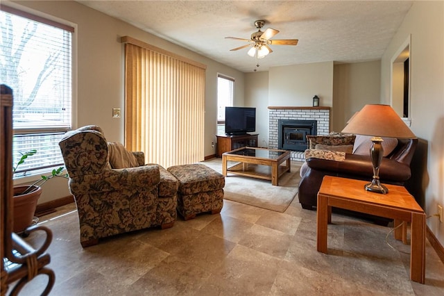 living room with a brick fireplace, a textured ceiling, baseboards, and ceiling fan