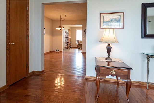 corridor with hardwood / wood-style floors, an inviting chandelier, baseboards, and visible vents