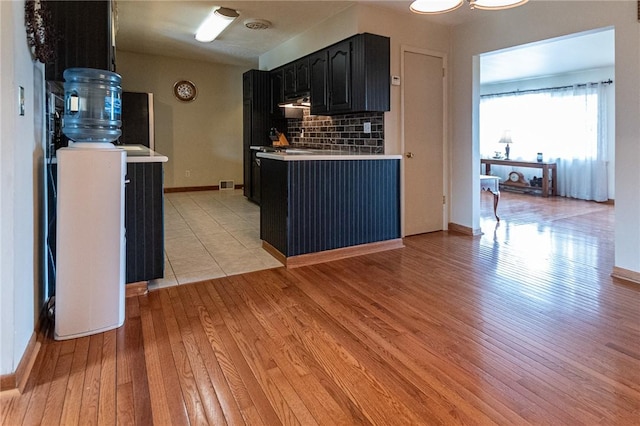 kitchen with dark cabinets, tasteful backsplash, light wood-type flooring, light countertops, and visible vents