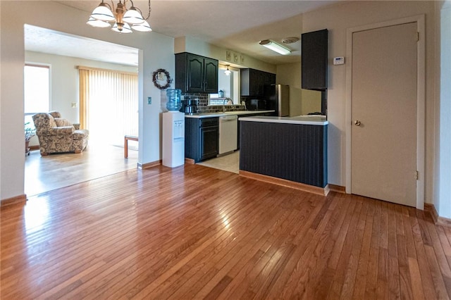 kitchen with white dishwasher, a notable chandelier, light countertops, freestanding refrigerator, and light wood finished floors