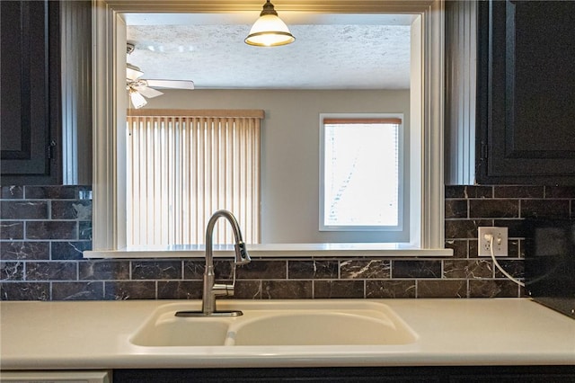 kitchen featuring dark cabinets, a textured ceiling, a ceiling fan, decorative backsplash, and a sink