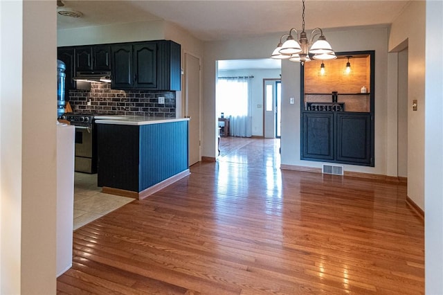 kitchen featuring range, light wood-type flooring, visible vents, light countertops, and backsplash