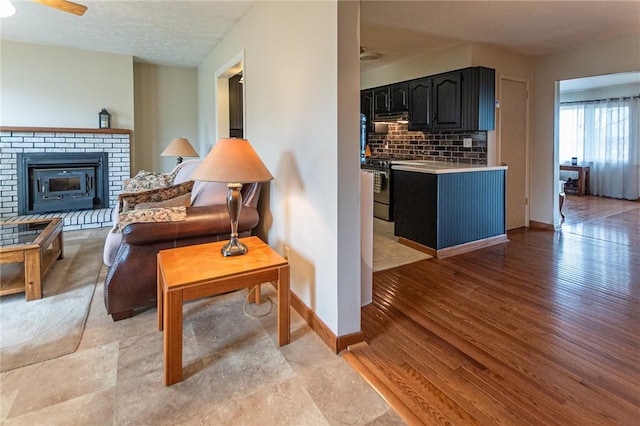 living area with baseboards, a textured ceiling, a ceiling fan, a brick fireplace, and light wood finished floors