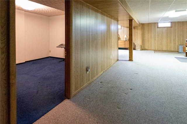 basement with wood walls, a paneled ceiling, and carpet flooring