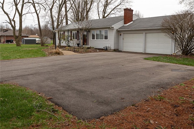 ranch-style home with a garage, aphalt driveway, a chimney, and a front lawn