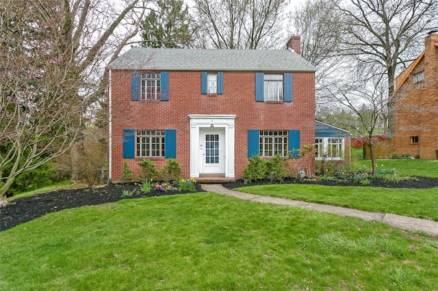 colonial-style house featuring brick siding, a front lawn, and a chimney