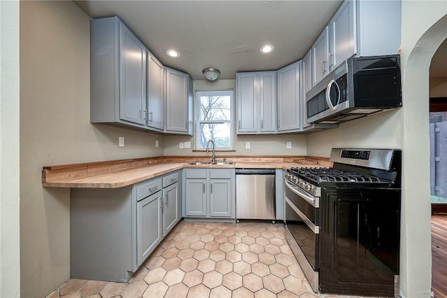 kitchen with gray cabinets, recessed lighting, stainless steel appliances, arched walkways, and a sink