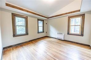 spare room featuring wood finished floors, a wall mounted air conditioner, baseboards, and vaulted ceiling