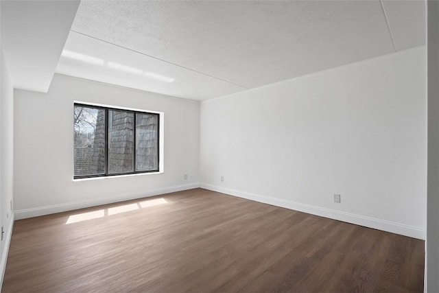 spare room with baseboards and dark wood-style floors