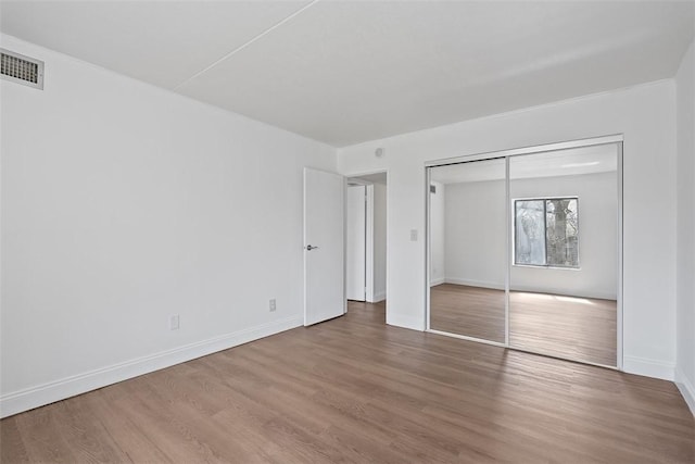 unfurnished bedroom with wood finished floors, baseboards, a closet, and visible vents