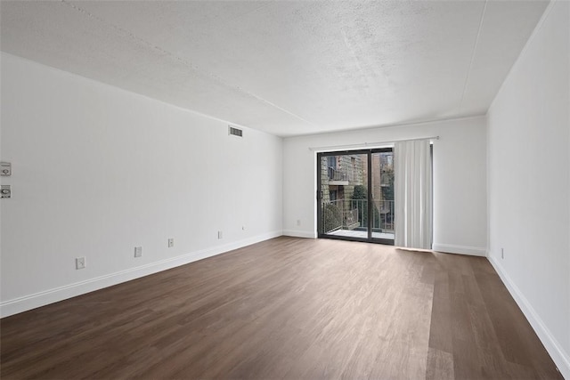 spare room with a textured ceiling, baseboards, dark wood-style floors, and visible vents