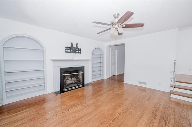 unfurnished living room with visible vents, built in shelves, ceiling fan, a fireplace, and wood finished floors
