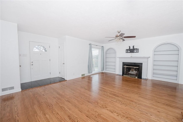 unfurnished living room with visible vents, built in shelves, a ceiling fan, and wood finished floors
