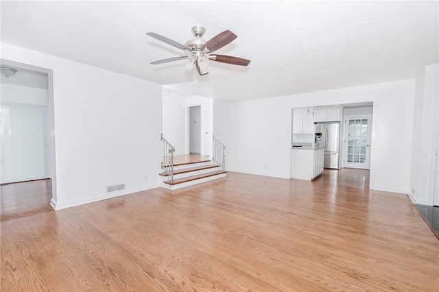 unfurnished living room featuring light wood finished floors, a ceiling fan, visible vents, and stairs