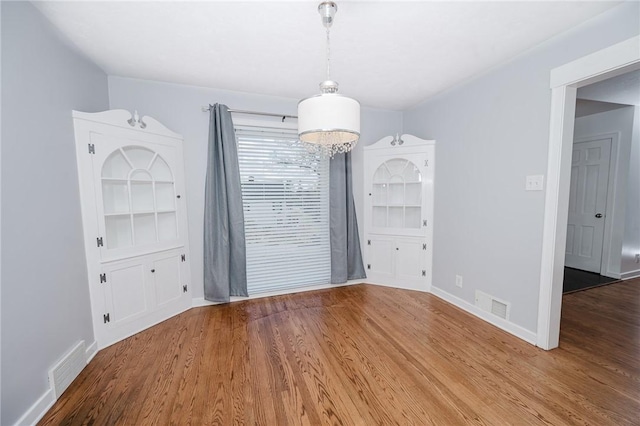 unfurnished dining area featuring wood finished floors, baseboards, and visible vents