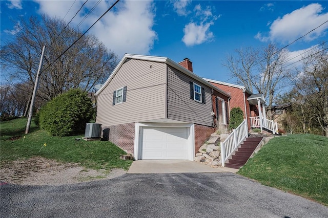 view of side of property featuring driveway, cooling unit, brick siding, a garage, and a yard