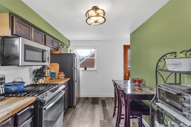 kitchen featuring baseboards, wooden counters, appliances with stainless steel finishes, dark brown cabinets, and wood finished floors