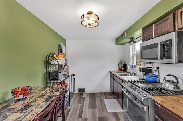 kitchen featuring dark brown cabinets, visible vents, appliances with stainless steel finishes, a sink, and wood finished floors