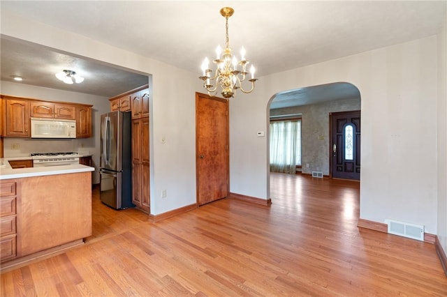 kitchen with white microwave, freestanding refrigerator, visible vents, arched walkways, and stove