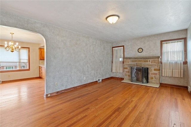 unfurnished living room with light wood-style flooring, a notable chandelier, a stone fireplace, and plenty of natural light