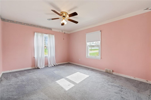 carpeted empty room featuring ceiling fan, baseboards, visible vents, and plenty of natural light