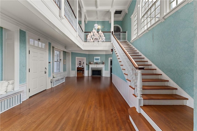 foyer entrance with a notable chandelier, a fireplace, a high ceiling, stairs, and wood finished floors