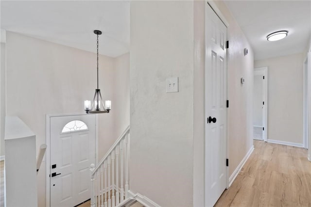 foyer entrance with a notable chandelier, light wood-style flooring, and baseboards