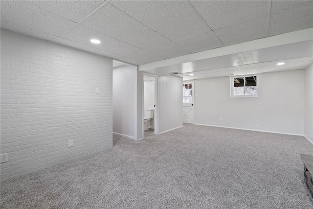 basement featuring brick wall, carpet flooring, a drop ceiling, and baseboards