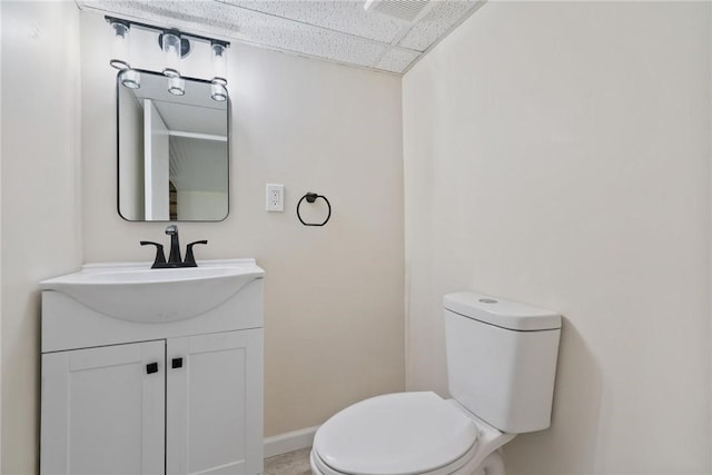 half bath featuring vanity, baseboards, visible vents, and toilet
