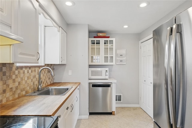 kitchen with glass insert cabinets, a sink, light countertops, appliances with stainless steel finishes, and white cabinetry