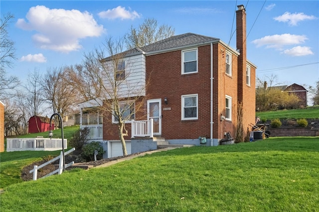 back of house featuring a chimney, cooling unit, an attached garage, brick siding, and a yard