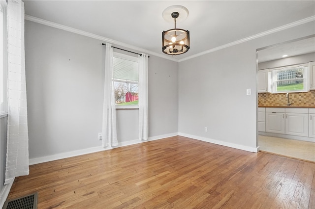 unfurnished dining area with visible vents, light wood-type flooring, an inviting chandelier, and ornamental molding