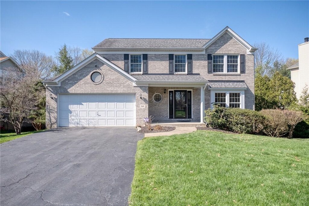 traditional home with an attached garage, driveway, a front yard, and brick siding