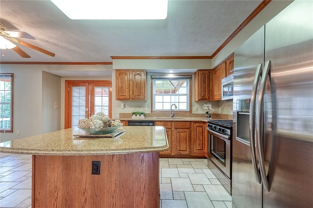 kitchen with brown cabinetry, ornamental molding, a kitchen island, a sink, and stainless steel appliances