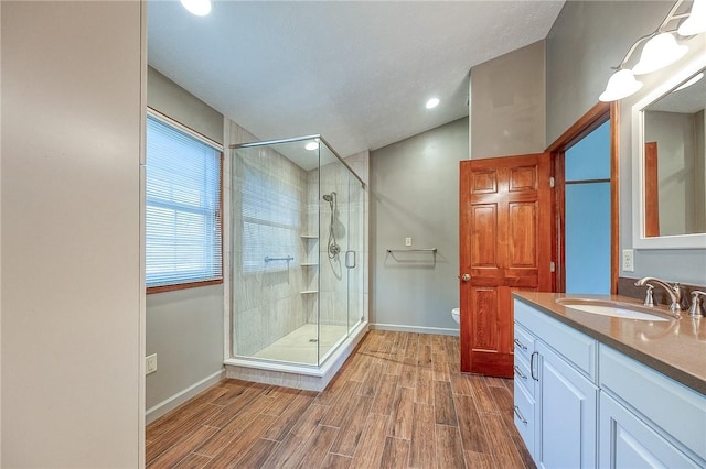 bathroom featuring vanity, toilet, wood tiled floor, a stall shower, and baseboards