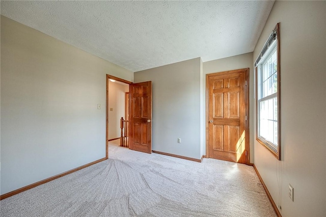 unfurnished bedroom with baseboards, light carpet, and a textured ceiling