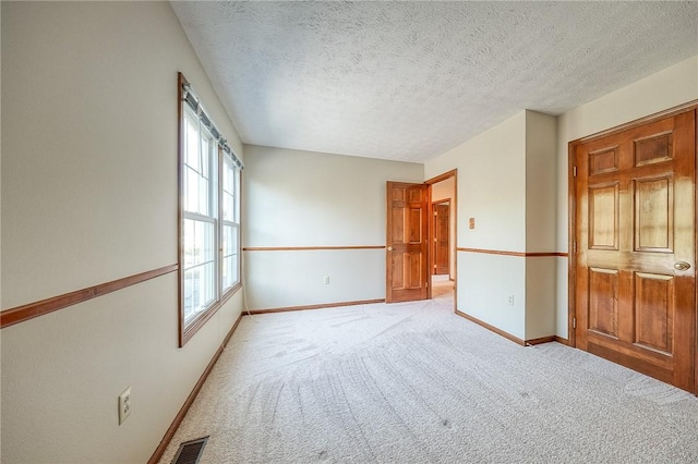 spare room featuring a textured ceiling, light colored carpet, baseboards, and visible vents